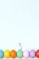 Top view of an Easter composition of painted eggs in bright juicy colors on a white background with a little rabbit. Holiday concept, flat layout, minimalism