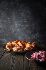 Fried potatoes with meat and red cabbage salad, on a black plate, on a black background
