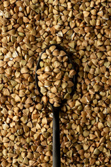Black metal spoon with buckwheat groats on buckwheat groats texture