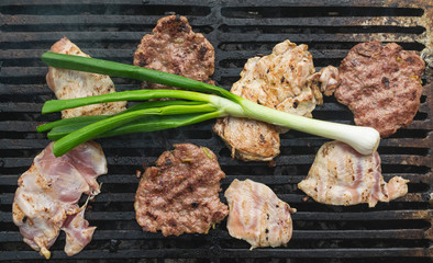 Burgers and chicken meat on barbecue along with vegetables