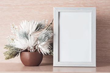 Photo frame and white flowers on a light wooden background, place for text.