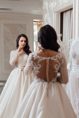 Fototapeta premium Attractive young bride choosing wedding dress in wedding salon. Bride in wedding dress posing. Sexy bride. Bride with luxurious hair and makeup.
