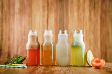 Four lemonade with strawberry, lemon, kiwi, apple, apricot, peach and mint in glass bottles on wooden background. Summer cold drink and beverages
