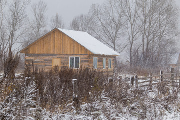 The village of Latin American Old Believers who returned to Russia in the Primorsky Territory. Wooden houses of Old Believers during a snowfall on a background of beautiful fields and mountains.