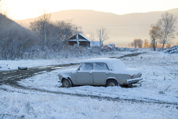 The village of Dersu in the Primorsky Territory, inhabited by the Old Believers. An old white Soviet car stands in the middle of a village during a snowfall.