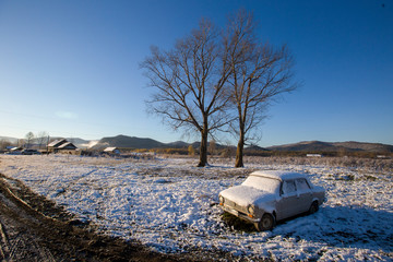 The village of Dersu in the Primorsky Territory, inhabited by the Old Believers. An old white Soviet car stands in the middle of a village during a snowfall.