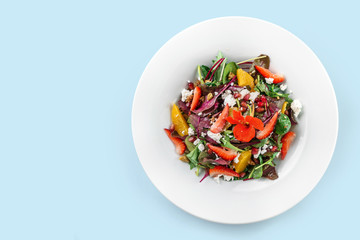 Healthy fresh salad with mix greens, strawberry, orange, nuts, cream cheese and edible flowers in plate isolated on blue background. Healthy food, vegetarian dieting, top view