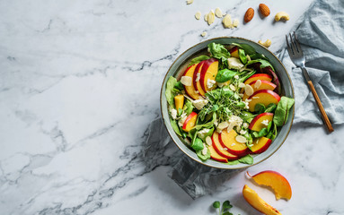 Fresh summer salad with peach, spinach, micro greens, feta cheese and almonds on light marble...