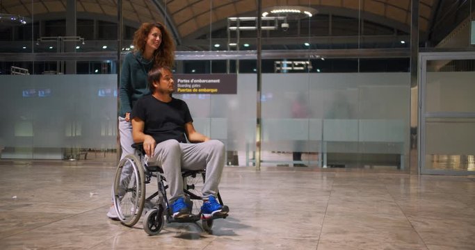 Happy disabled man in a wheelchair with happy young woman running at the airport.