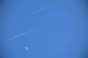Two Jets in Blue Sky with Contrails Flying Past Half Moon