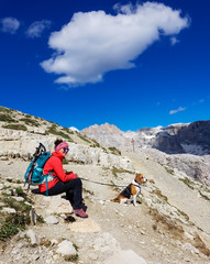 Young woman with a beagle dog trekking in a mountain range in Italian Alps. Sitting on a rock and enjoying nature.