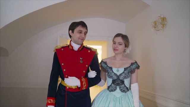The guy in uniform invites the girl to dance. Love story guy invites a girl in an old, beautiful dress to dance. A guy and a girl in clothes from the 19th century.