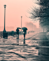 Two people walking in the fog and rain with a pink sky.