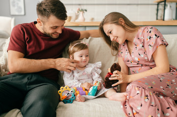 Pretty caucasian mother and strong father in a bright room with his cute little daughter sit on a chair and enjoy the pastime