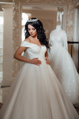Naklejka premium Long hair. Makeup. Beautiful girl portrait. Brunette fashion woman with manicured nails, healthy curly shiny hairstyle posing. Bride at the salon in wedding dress. 