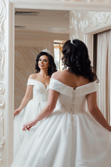 Fototapeta premium Bride at the salon in wedding dress. Beautiful model girl with elegant hairstyle. Fashion. Beautiful and fashion bride in luxury interior. Bride is looking into the mirror