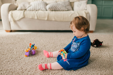 Little cute girl in beautiful dress sits on the floor, carpet and plays with her various toys