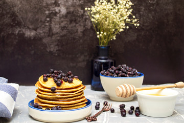 Pancakes with blueberries and honey on a plate. Pancakes and a spoon for honey.