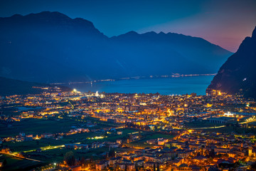 Fototapeta premium Arial Panorama of the gorgeous Garda lake surrounded by mountains in the in the autumn by night, View of the beautiful Riva del Garda town and Garda lake