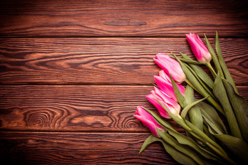 Bouquet of pink tulips on brown wooden background.
