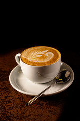A Cup of cappuccino with a pattern on the foam is on the table in the early morning, while it is...
