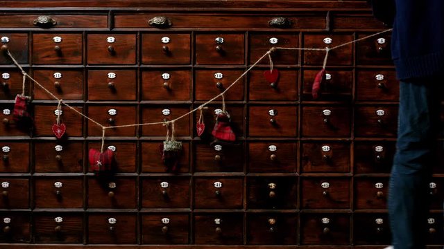 Vintage, dark wood apothecary cabinet with many drawers. Christmas garland decoration is hung on the drawer knobs. Cute holiday clip.