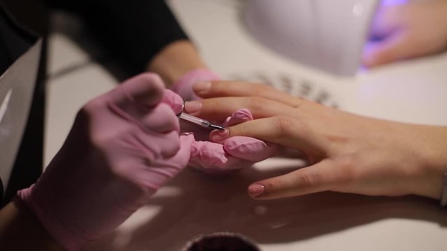 Closeup of women paints nails. Manicure nail art. Female works in pink gloves. Close up of woman's hands