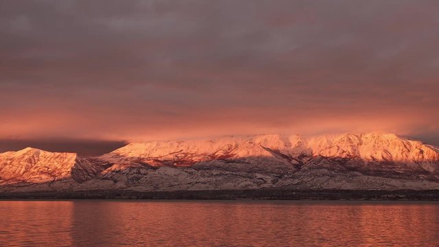 Snow covered mountain glowing during sunset reflecting in lake in Utah Valley in winter.