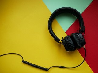 Classic black wired headphones on colored paper background. Retro style. 80s. Pop culture. Top view.