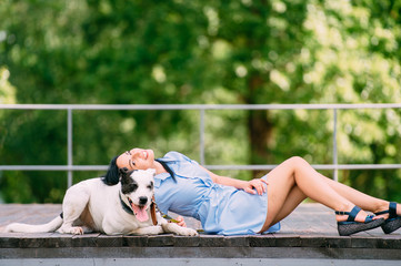 Beauteous woman sits with her lovely dog on the bridge in the park and rejoices