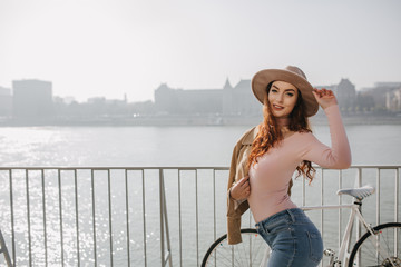 Shapely long-haired woman in pink shirt posing with pleased smile on nature background. Outdoor...