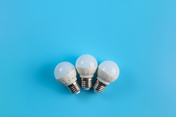 Three small white led energy saving led light bulbs on a blue background.