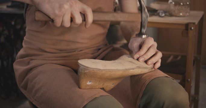Traditional bespoke shoemaker nailing leather insole on wooden shoe last in workshop
