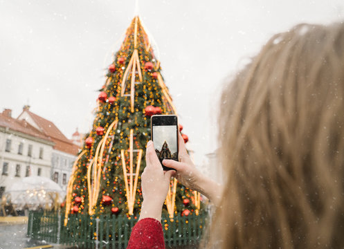 Crop view of woman taking photo of Christmas tree with smartphone on a snowy day