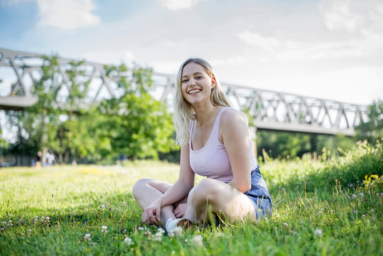 Portrait Of Happy Young Woman Relaxing On A Meadow In Summer, Berlin, Germany