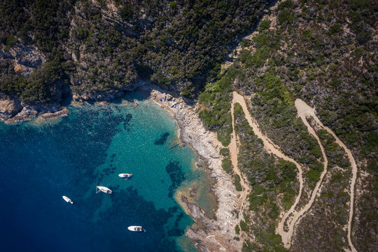 Italy, Province of Livorno, Elba, Aerial view of winding road and boats floating in blue coastal water