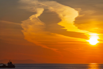 Colorful cloudy sunset over the sea with a commercial ship at the left of frame in Mykonos,...