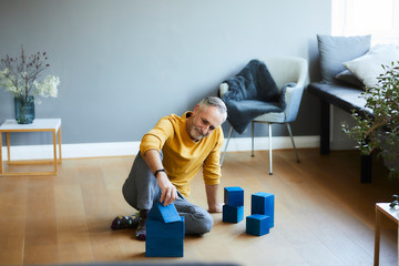Mature man playing with building blocks on the floor at home