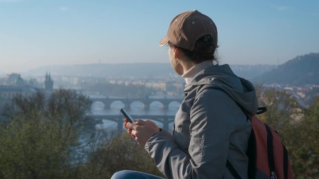 Tourist with a smartphone on the observation deck. A cute girl tourist with a phone looks at the panorama of the Paris bridges.