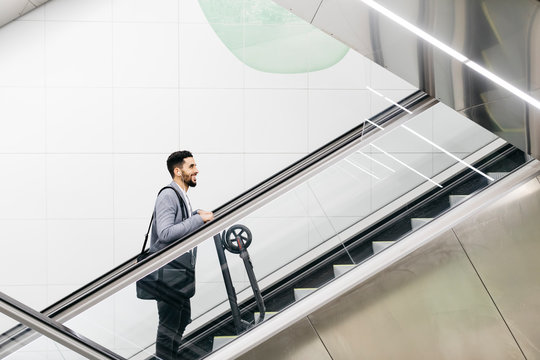 Smiling young businessman with electric scooter on escalator