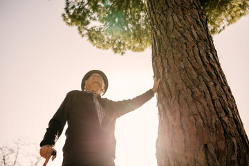 Old man with cane, leaning on tree in park