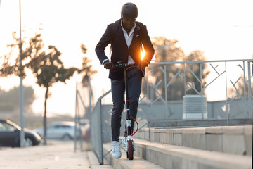 Young businessman with backpack and cycling helmet riding push scooter at sunset