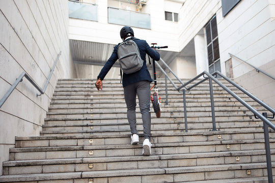 Back view of businessman with push scooter walking upstairs