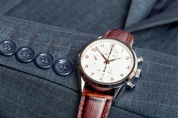 strict designed men's wristwatch with brown leather strap, on the suit of gray fabric close up...