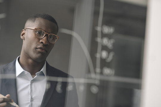 Portrait of young businessman looking at diagram on glass pane in office