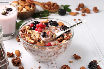 Granola crispy honey muesli with natural yogurt, fresh berries, chocolate and nuts in a bowl against a light background, healthy food