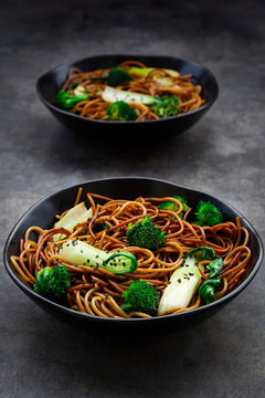 Two bowls of soba noodles with pak choi and broccoli, soy sauce and black sesame