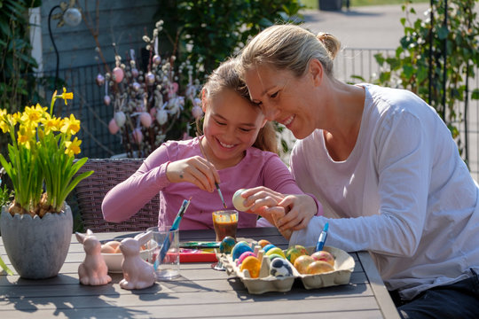 Happy mother and daughter sitting at garden table painting Easter eggs