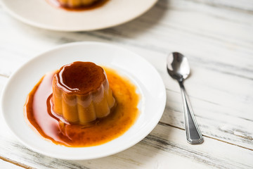 Close up of a flan creme caramel pudding with mint, a custard dessert against white wooden background
