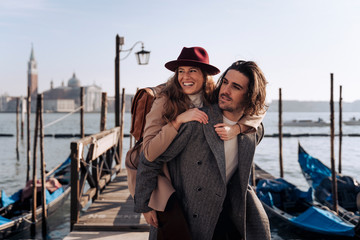 Young man giving his girlfriend a piggyback ride at the waterfront in Venice, Italy